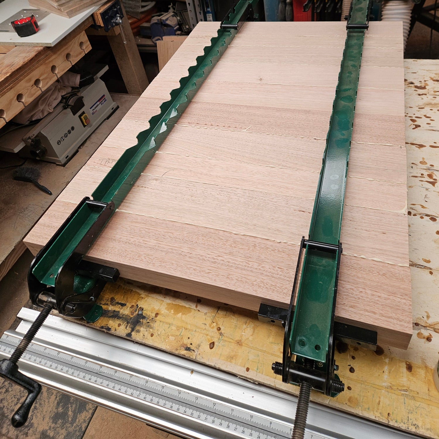 Wooden panel clamped in a woodworking machine with a workshop background