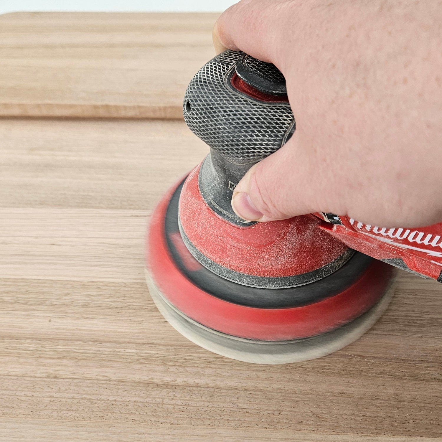 Person using a Milwaukee sander on a wooden surface